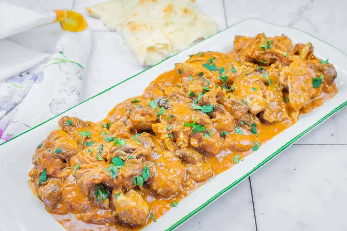 A rectangular plate of Chicken Tikka Masala with herbs on top.