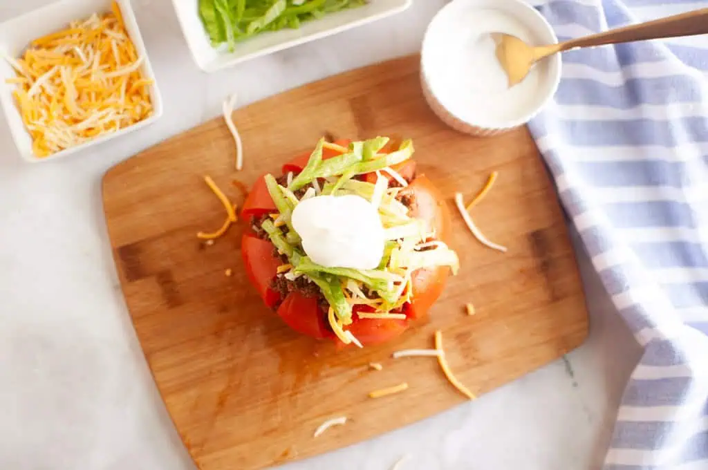 A ripe red tomato, hollowed out and filled with taco meat and toppings, on a white plate.