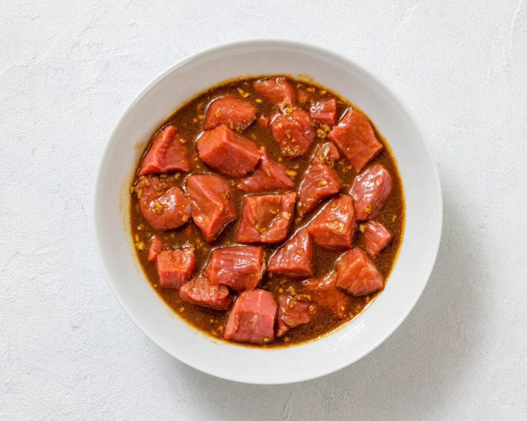 A white bowl filled with chunks of raw fish marinating in a brown sauce, viewed from above on a light-colored surface.