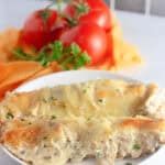 A plate of White Chicken Enchiladas, garnished with parsley, with fresh tomatoes and herbs in the background.