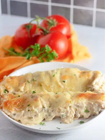 A plate of White Chicken Enchiladas, garnished with parsley, with fresh tomatoes and herbs in the background.