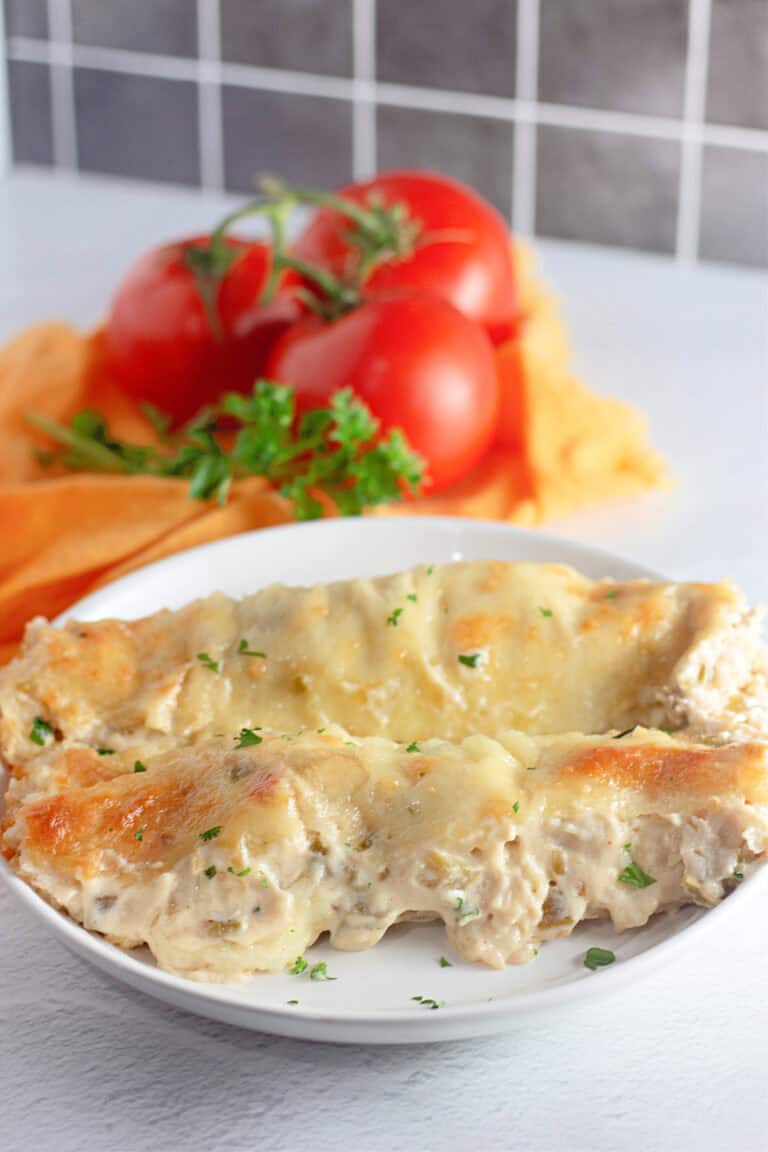 A plate of White Chicken Enchiladas, garnished with parsley, with fresh tomatoes and herbs in the background.
