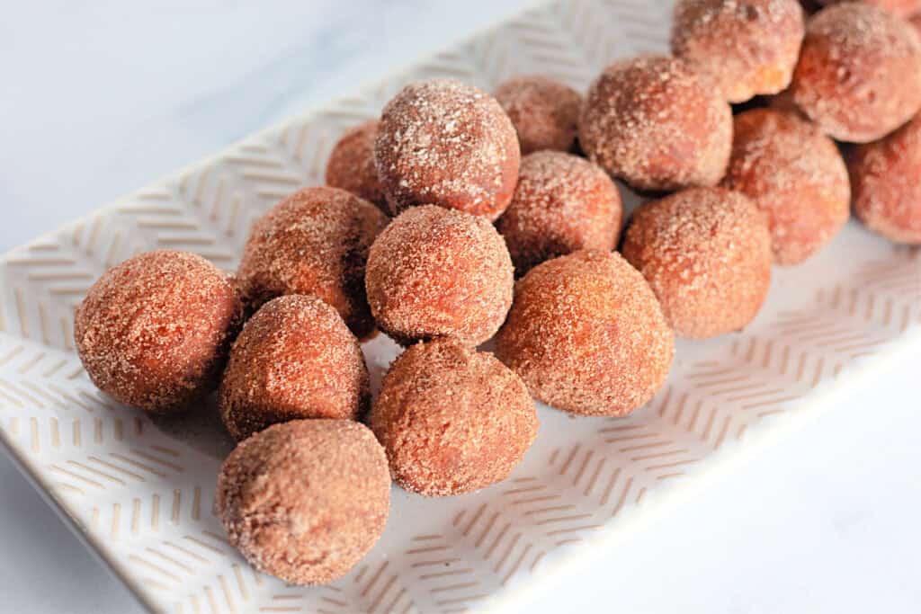 A rectangular plate holds several round donut holes coated in cinnamon sugar.