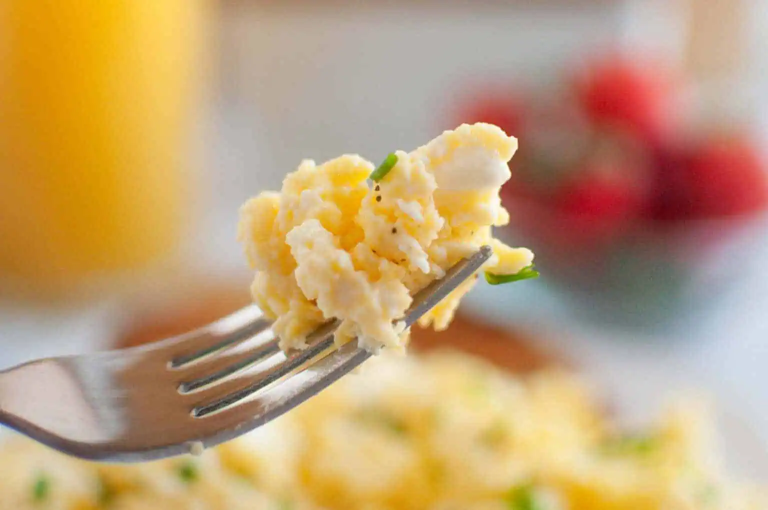 A close-up of a fork holding a bite of scrambled eggs garnished with chopped chives.