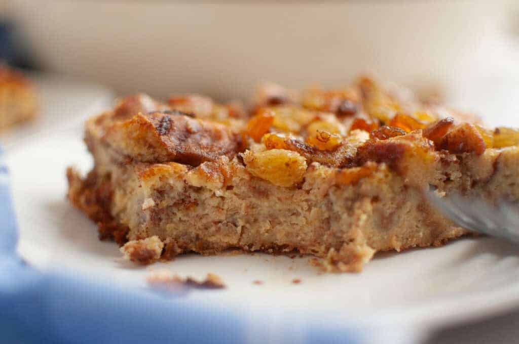 A close-up of a slice of Cinnamon Roll Casserole topped with golden raisins on a white plate.
