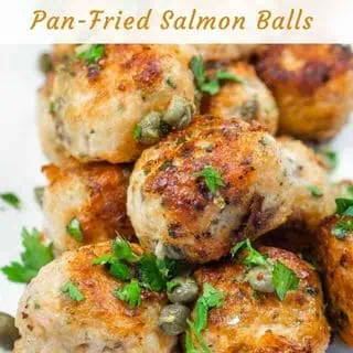 A close-up of a stack of golden-brown meatballs garnished with capers and fresh parsley.