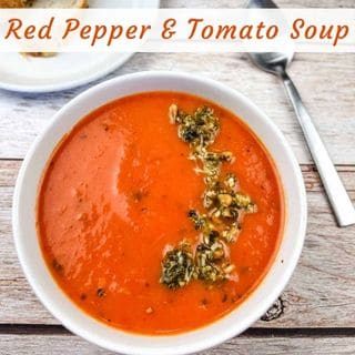 A white bowl of red pepper and tomato soup, garnished with pesto.
