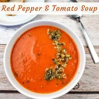 A white bowl of red pepper and tomato soup, garnished with pesto.