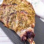 A whole roasted leg of lamb seasoned with herbs on a black serving platter.