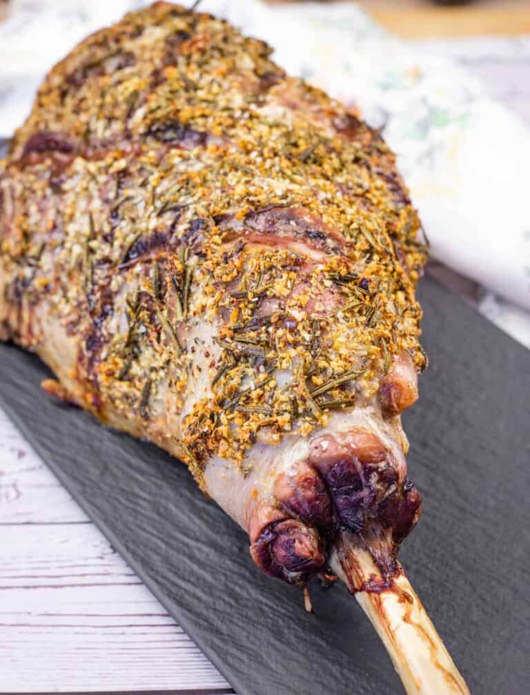 A whole roasted leg of lamb seasoned with herbs on a black serving platter.