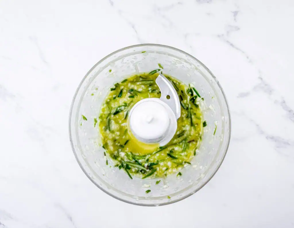 Overhead shot of chopped basil, garlic, and olive oil being processed in a food processor.