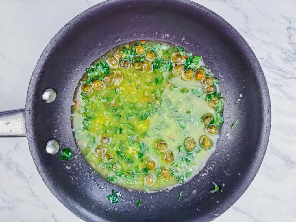 Overhead shot of a lemon-caper sauce with fresh parsley in a black pan.