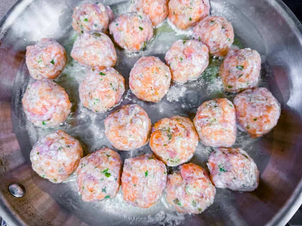 Overhead shot of raw salmon balls cooking in a pan.