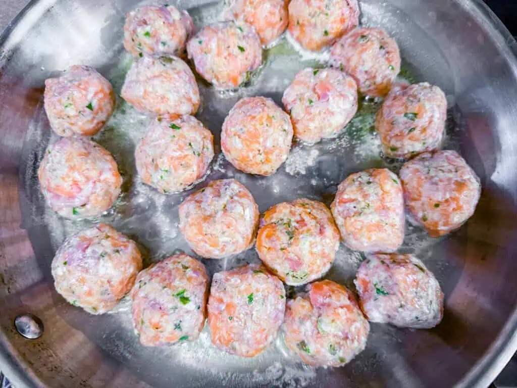 Overhead shot of raw salmon balls cooking in a pan.