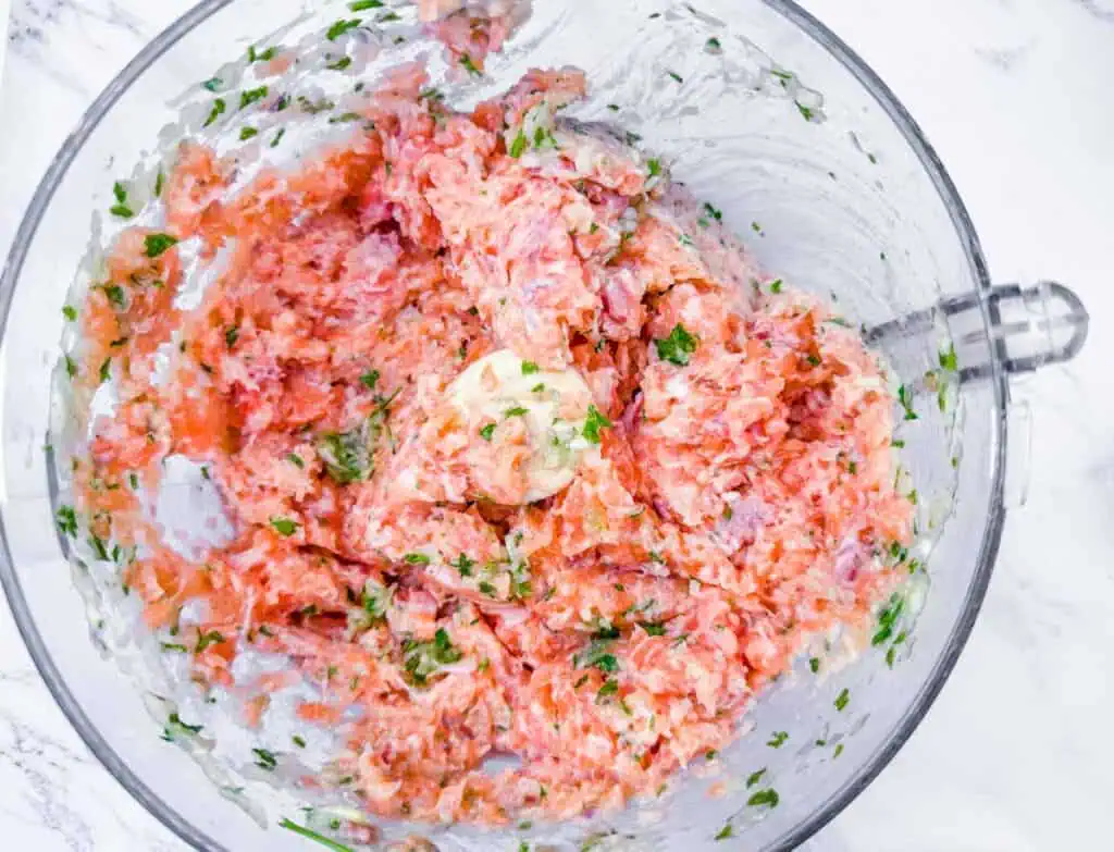Overhead shot of raw salmon being processed with herbs and other ingredients in a food processor.