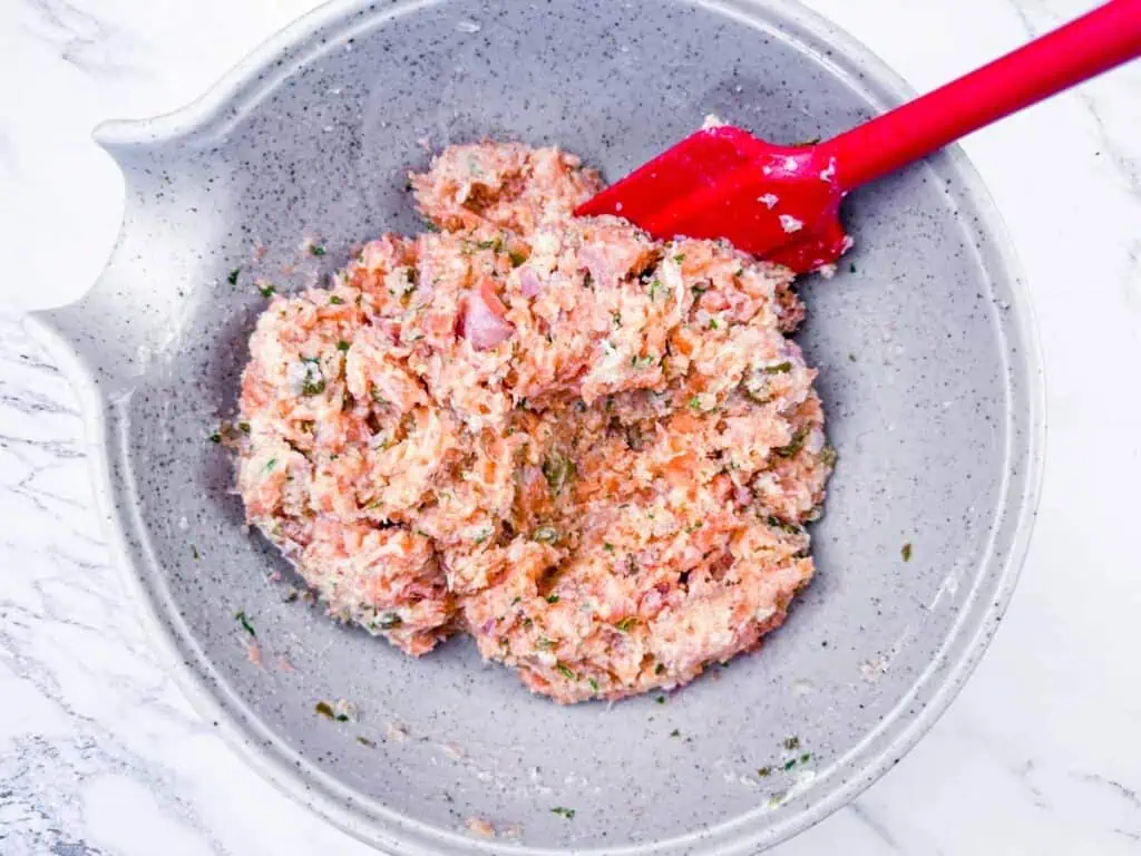 Overhead shot of raw salmon mixture being stirred with a red spatula in a gray bowl.