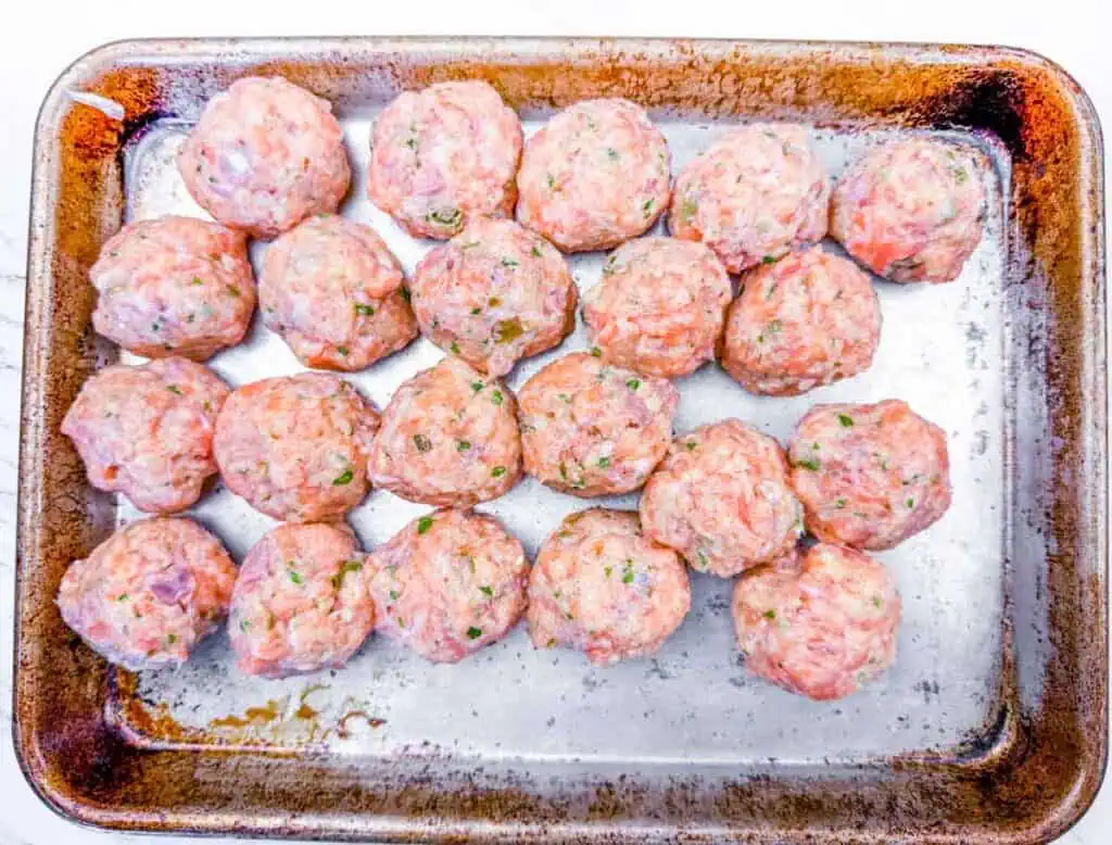Overhead shot of rows of raw turkey meatballs on a greased metal baking sheet.