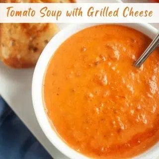 A bowl of tomato soup with a spoon next to a piece of grilled cheese sandwich on a white plate.