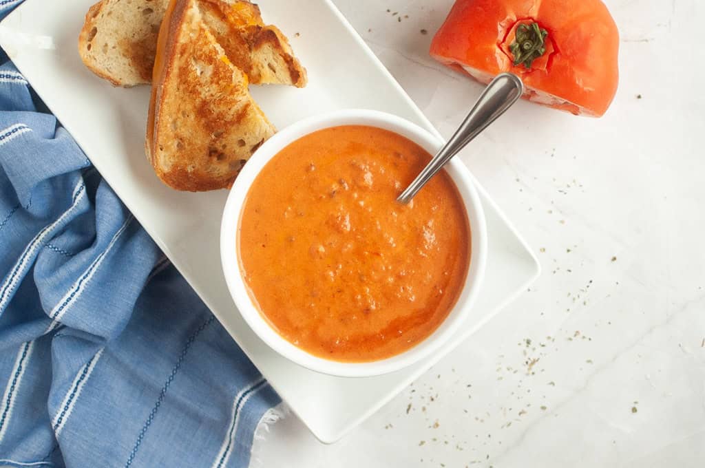 Overhead shot of a bowl of creamy tomato soup with a spoon, served with grilled cheese.