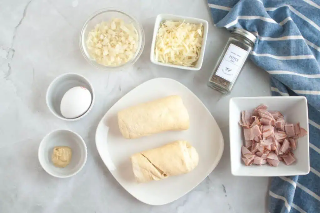 Overhead shot of ingredients for Ham & Cheese Puffs, including dough, ham, cheese, onion, egg, mustard, and pepper.