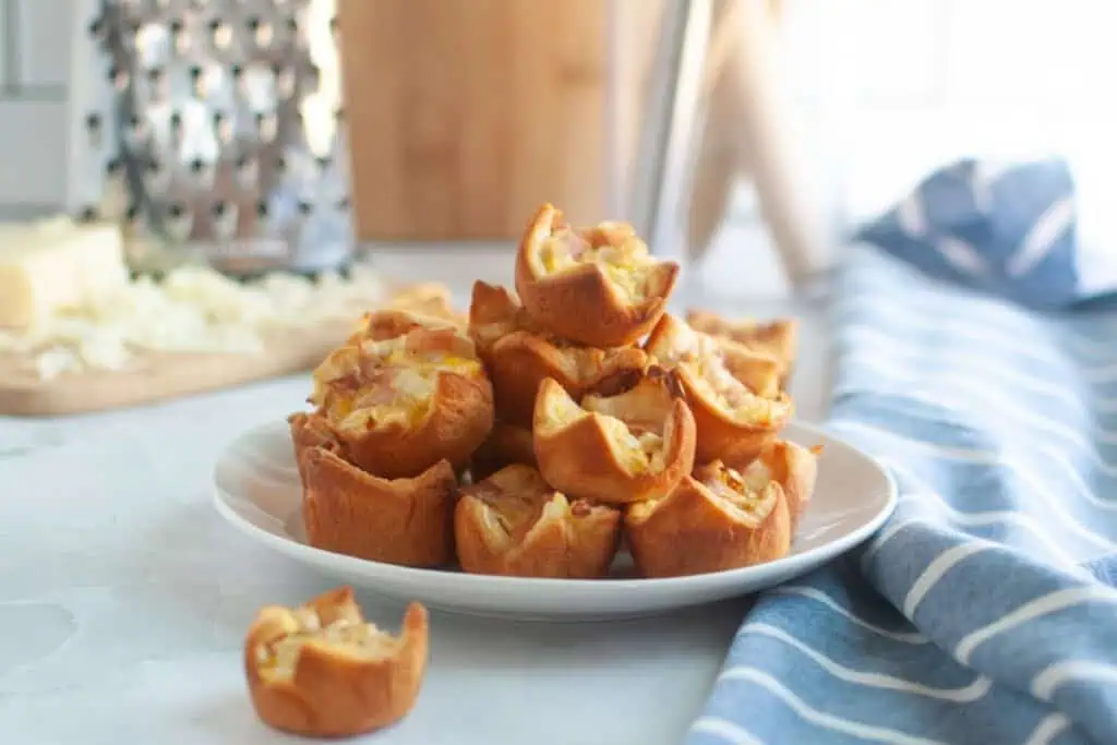 A white plate piled with small, golden-brown Ham and Cheese Puffs.