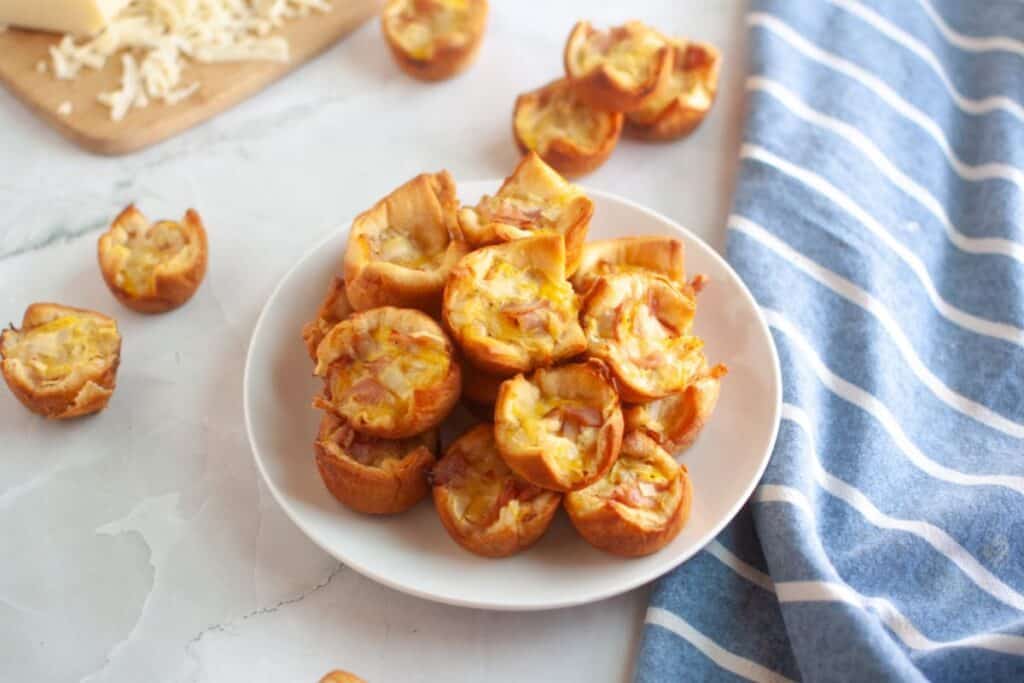 A white plate piled with small, golden-brown ham and cheese puffs.