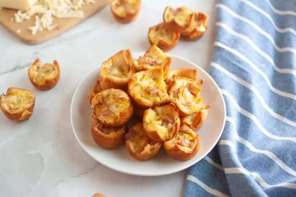 A white plate piled with small, golden-brown ham and cheese puffs.