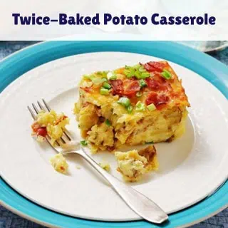 A serving of twice-baked potato casserole topped with chopped green onions and bacon sits on a white plate with a fork.