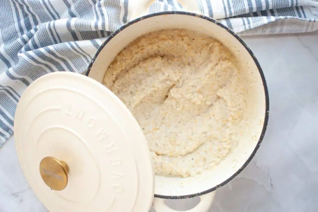 A pot of cooked oatmeal with the lid partially open sits on a marble countertop next to a blue and white striped cloth.