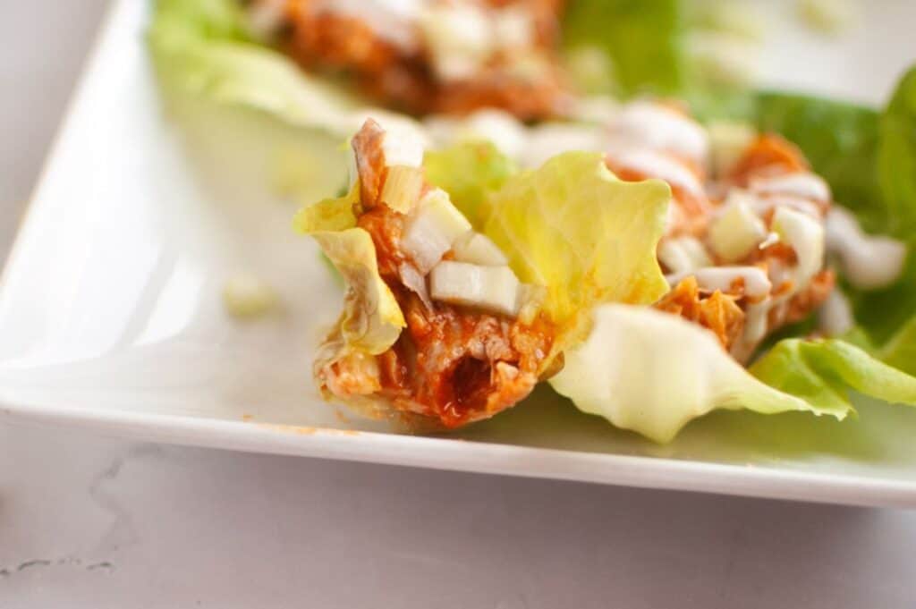 Close-up of a lettuce leaf filled with shredded meat, diced onions, and sauce, placed on a white plate.