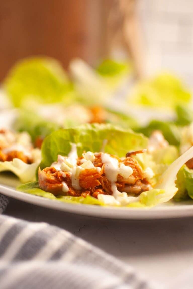 A close-up of Buffalo Chicken lettuce wraps filled with shredded chicken and topped with a white sauce, arranged on a white plate.