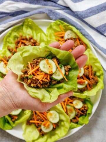 A hand holding lettuce cups filled with meat and vegetables.