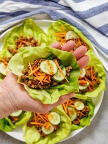 A hand holding lettuce cups filled with meat and vegetables.