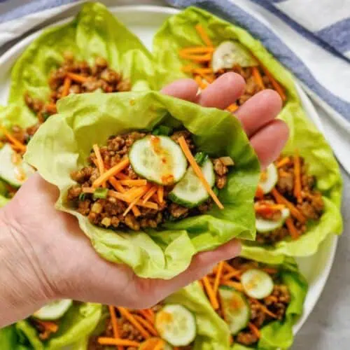 A hand holding lettuce cups filled with meat and vegetables.