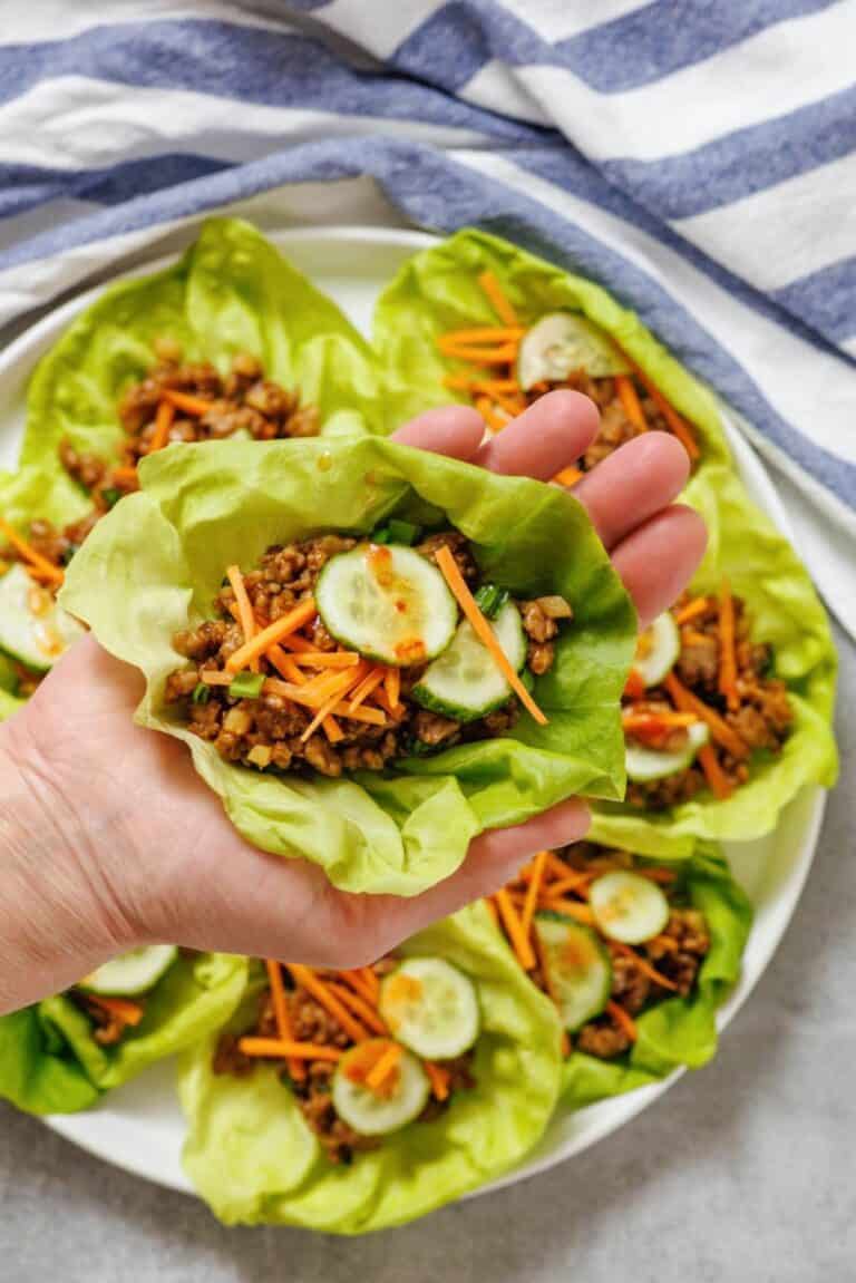A hand holding lettuce cups filled with meat and vegetables.