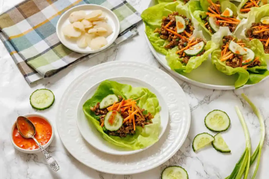 Lettuce wraps with meat and vegetables on a white table.