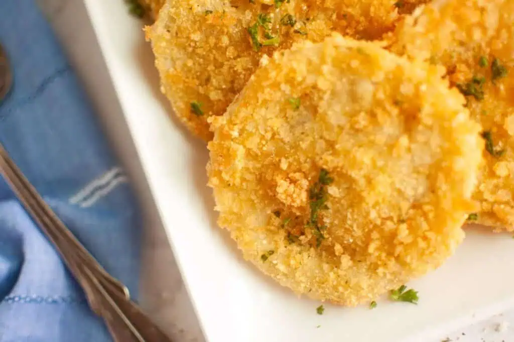 A plate of fried tomatoes with a fork and a bowl of sauce.