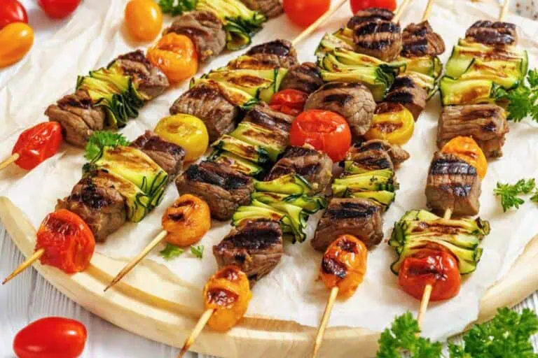 Grilled skewers with beef, zucchini slices, and cherry tomatoes are arranged on a wooden platter, garnished with parsley.