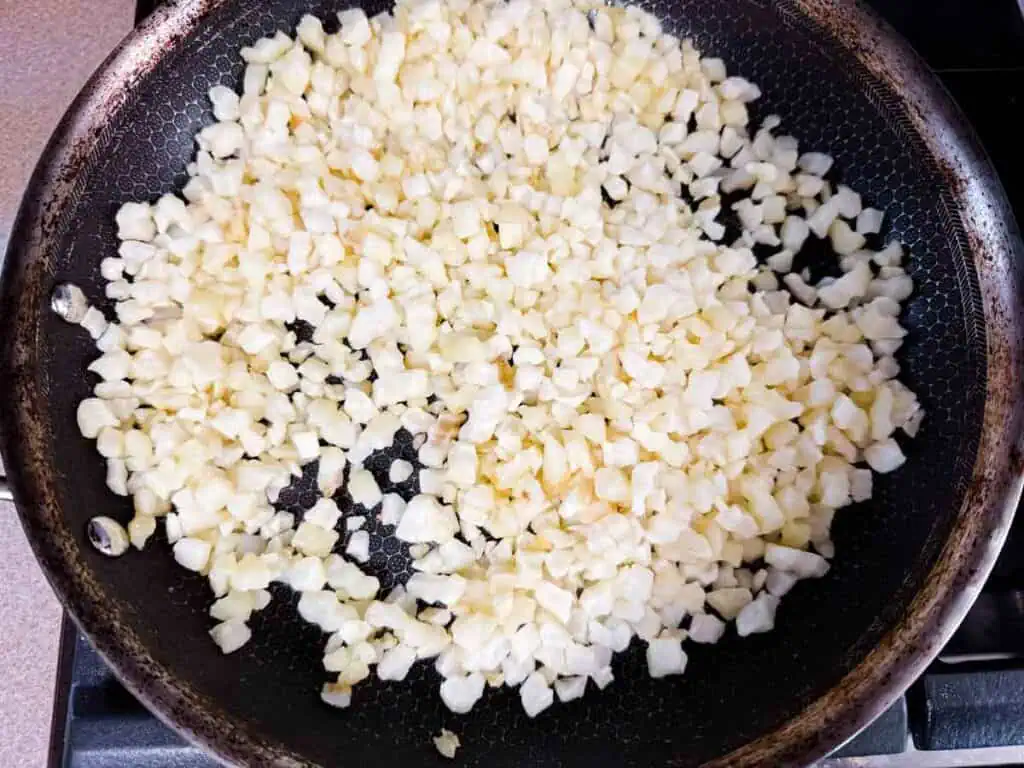 Diced cauliflower cooking in a black frying pan on a stovetop.