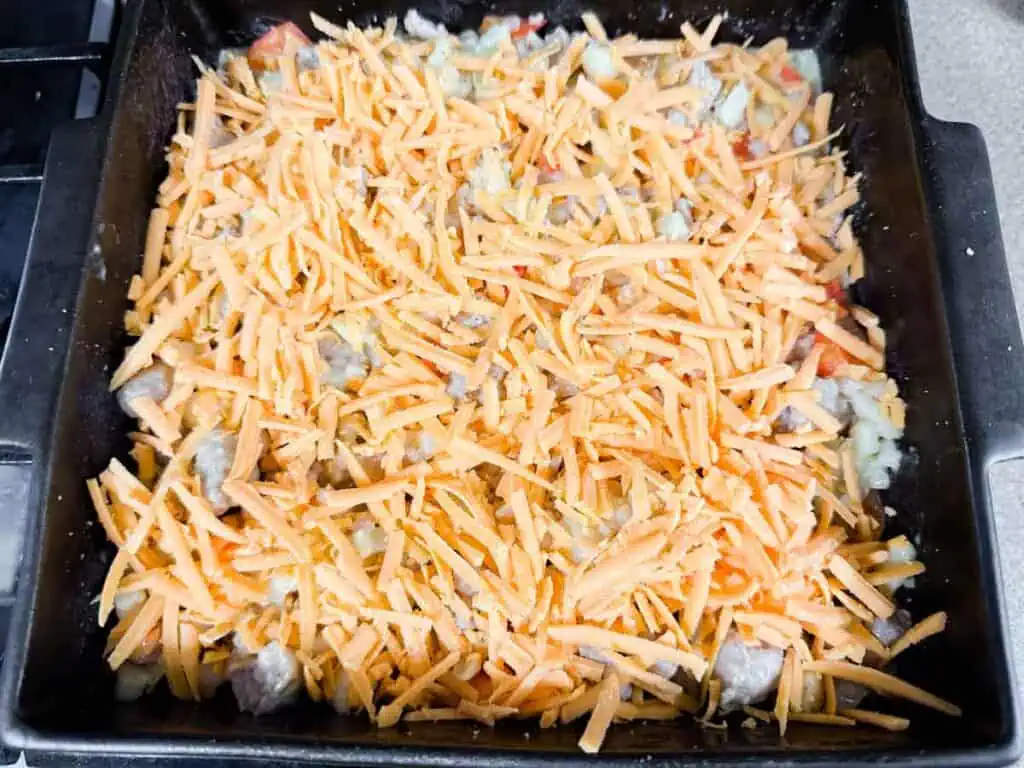 A baking dish filled with a mixture of chopped vegetables and meat, topped with a generous layer of shredded cheddar cheese.