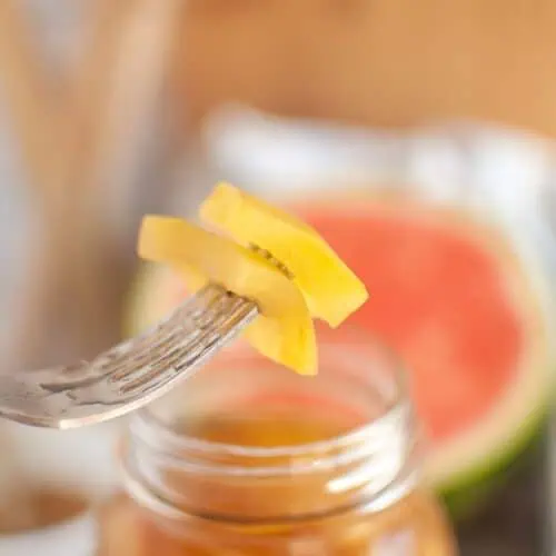 A fork is holding a piece of watermelon on a jar.