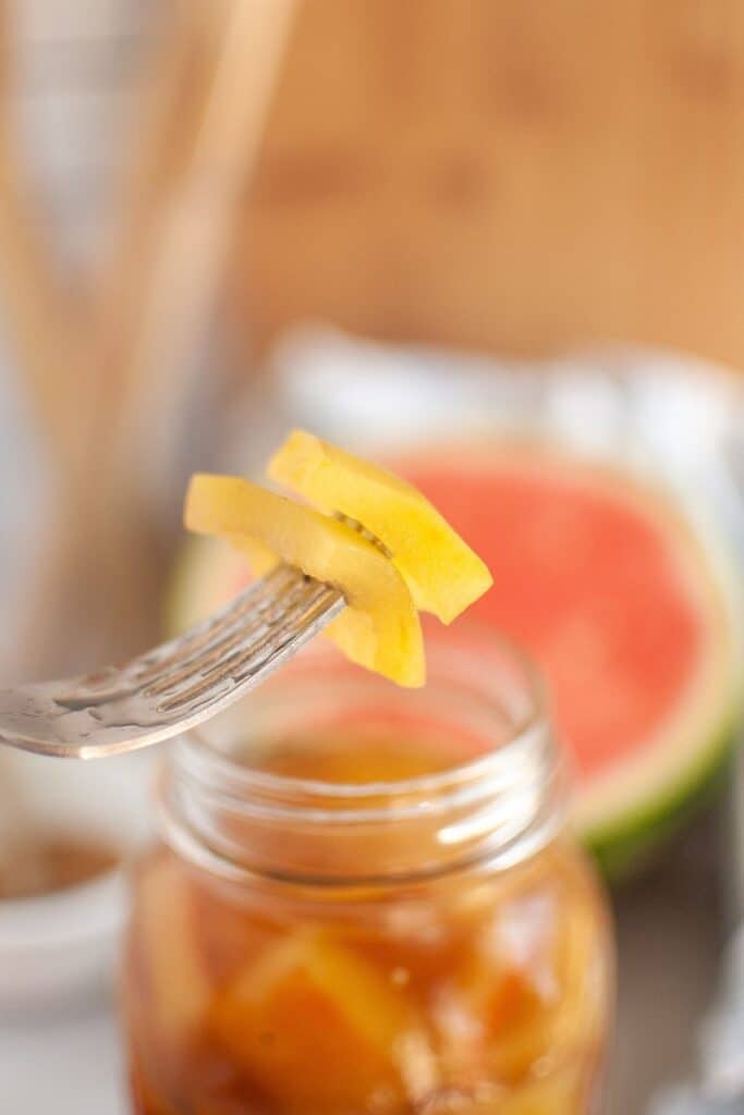 A fork is holding a piece of watermelon on a jar.
