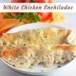 Two white chicken enchiladas covered in creamy sauce and melted cheese are served on a white plate, with a garnish of parsley, tomatoes, and an orange napkin in the background.