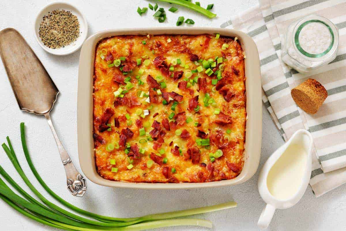 Grandma&rsquo;s Twice-Baked Potato Casserole topped with chopped green onions and bacon, surrounded by fresh green onions.