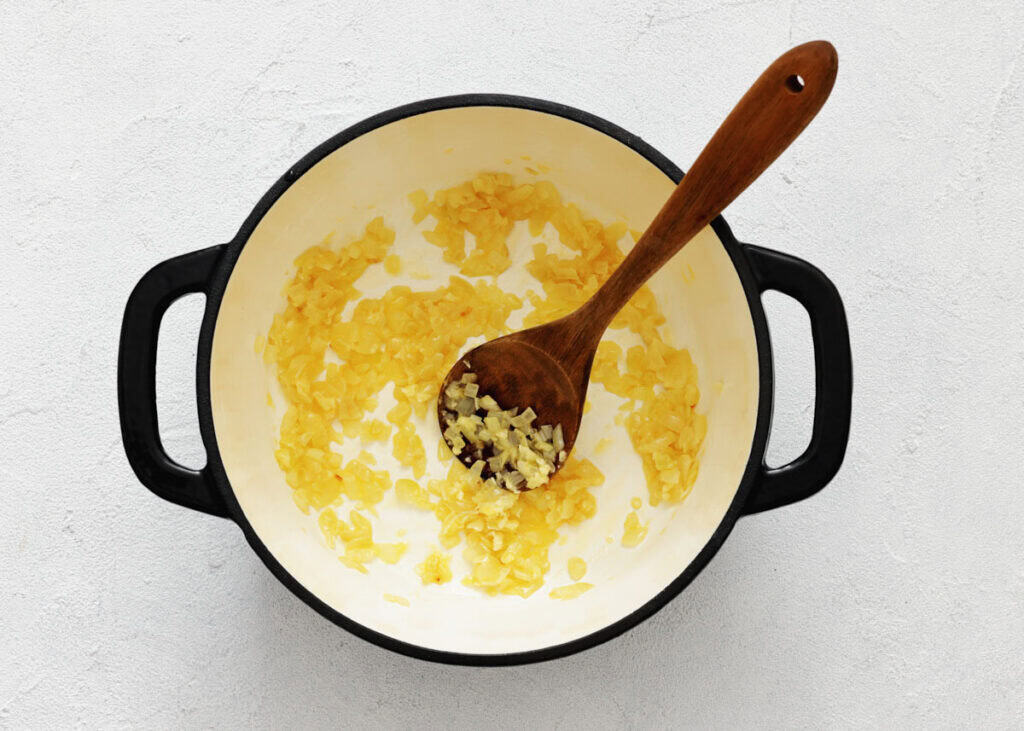 Chopped onions being saut&eacute;ed in a white pot with a wooden spoon.