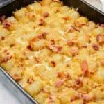A casserole dish filled with baked tater tots, melted cheese, and pieces of cooked bacon on top.