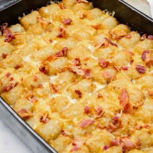 A casserole dish filled with baked tater tots, melted cheese, and pieces of cooked bacon on top.