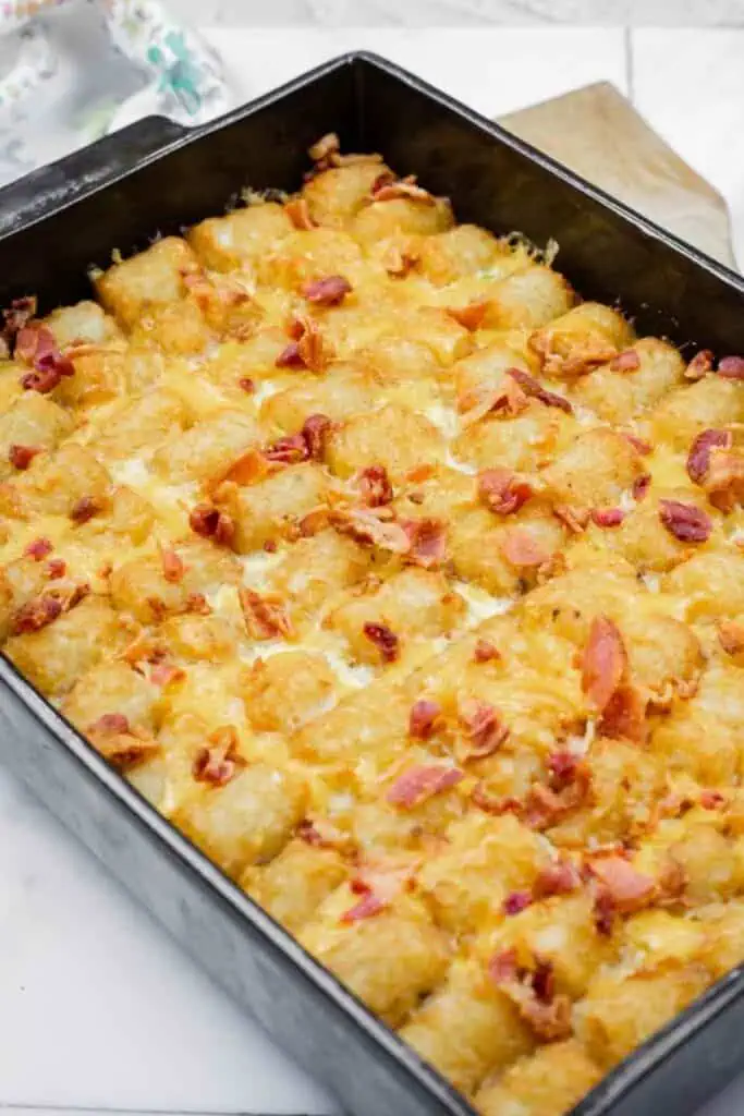 A casserole dish filled with baked tater tots, melted cheese, and pieces of cooked bacon on top.