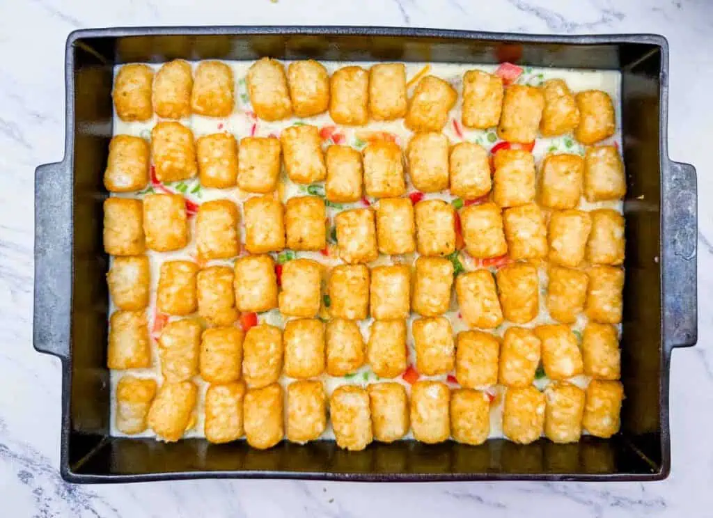 Rectangular baking dish filled with a creamy mixture topped with evenly arranged golden tater tots, ready to be baked.