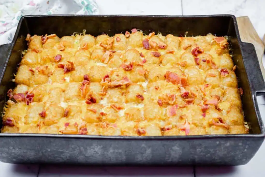 A baked casserole topped with golden tater tots, melted cheese, and pieces of cooked bacon in a rectangular pan.